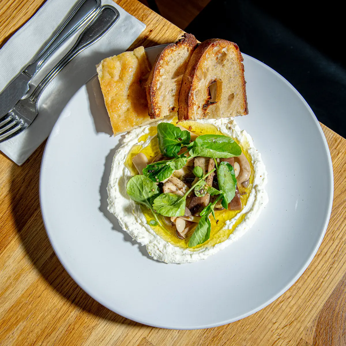 Sourdough toast topped with greens and avocado on a white plate